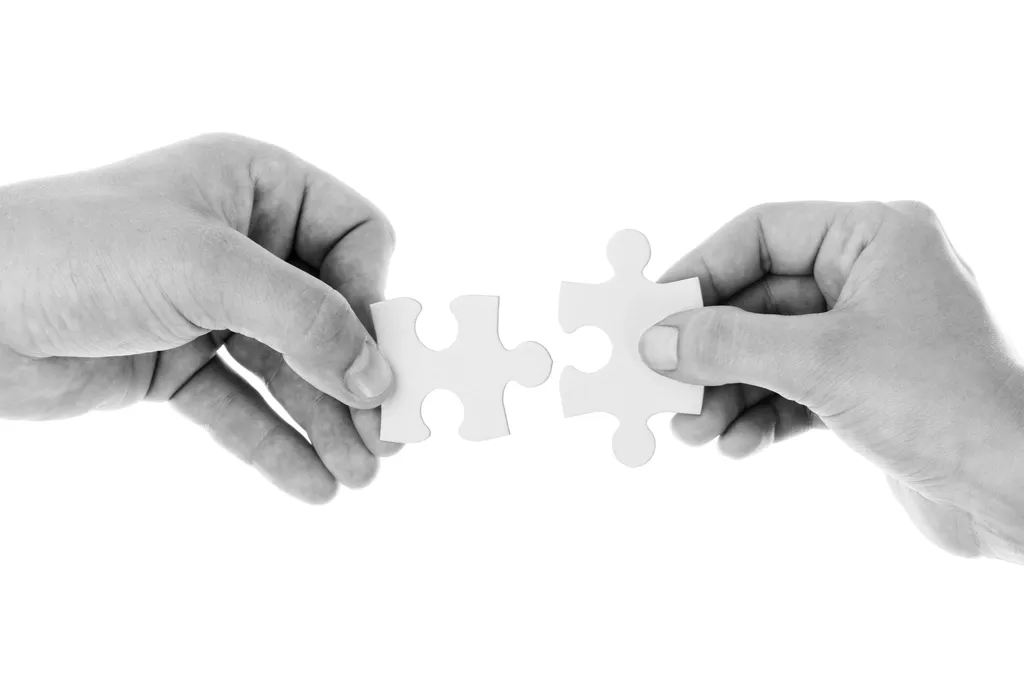 Deux mains assemblant deux pièces de puzzle, en noir et blanc