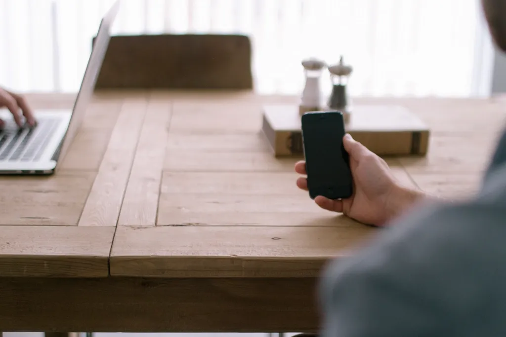 Main tenant un smartphone à côté d'un ordinateur portable sur une table en bois