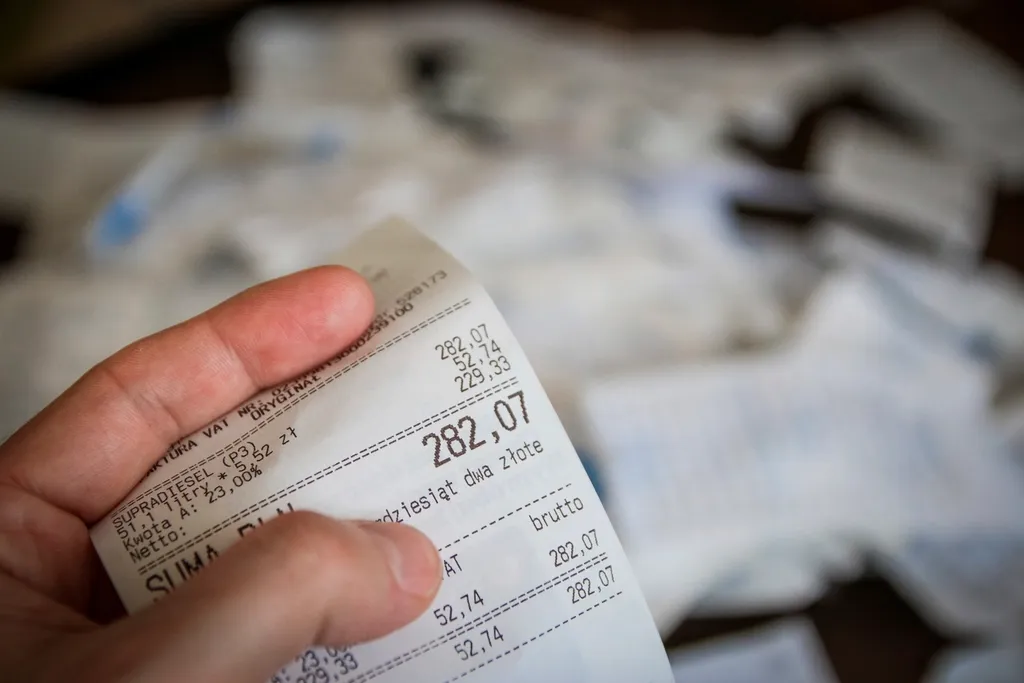 Hand holding a till receipt above a pile of receipts