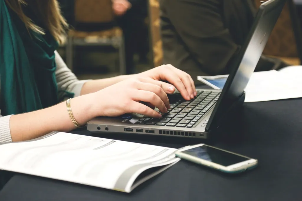 Mains sur le clavier d'un ordinateur portable, avec des notes et un téléphone