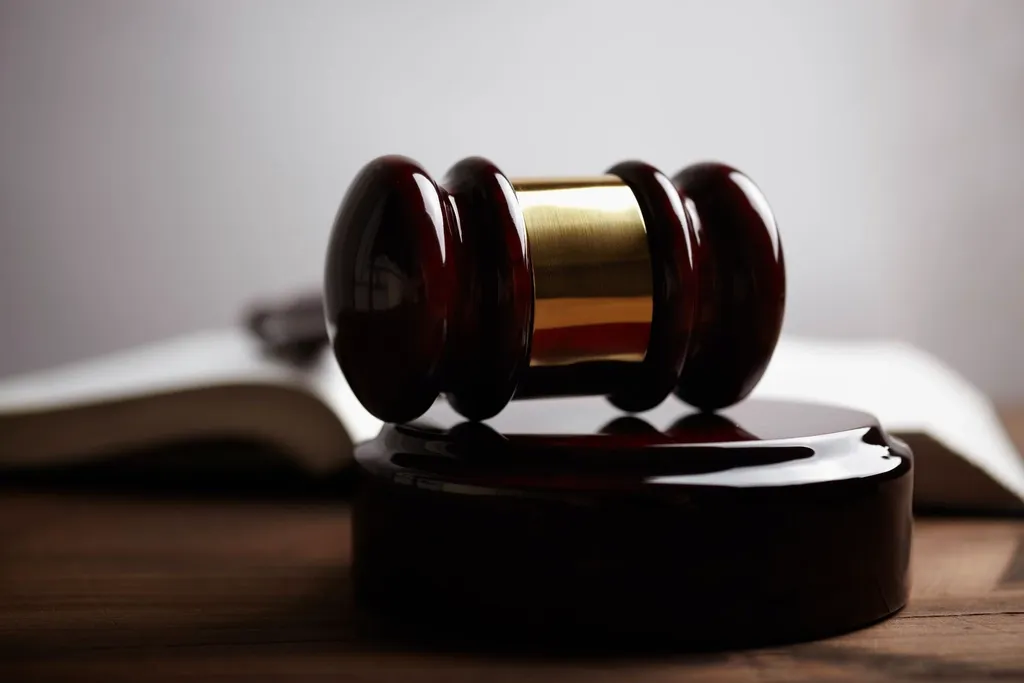 Marteau de juge en bois sombre posé sur son socle, livre ouvert en arrière-plan
