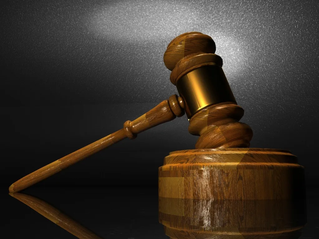 Marteau de juge en bois posé contre son socle rond, sur fond sombre