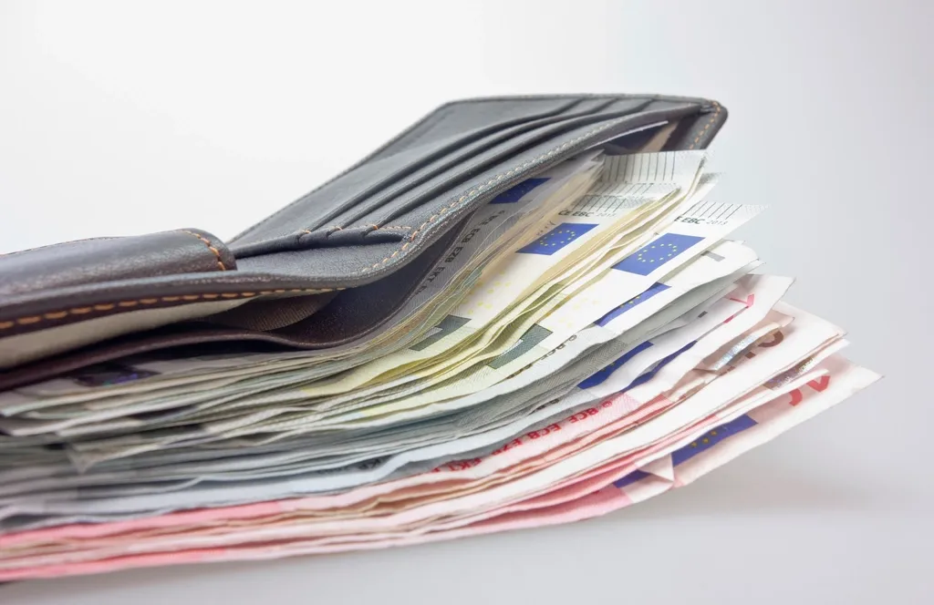 Portefeuille en cuir rempli de billets, posé sur une table claire