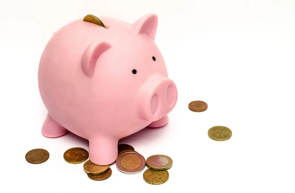Tirelire cochon rose entourée de pièces de monnaie