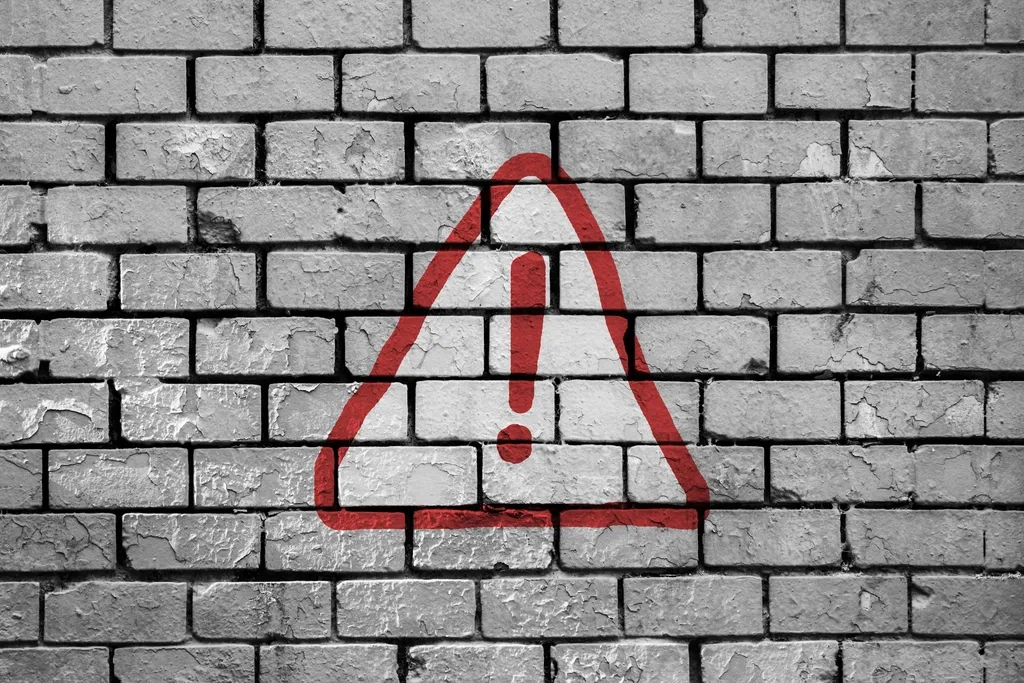 Red warning triangle painted on a white brick wall